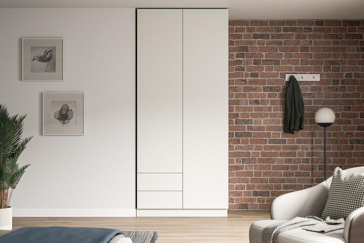 Eleganter Schrank nach Maß in modernem Wohnambiente Großer, maßgeschneiderter weißer Schrank im Kontrast zu einer Ziegelwand, neben Kunstwerken und einer stilvollen Stehlampe.